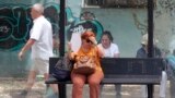 FILE - A woman tries to cool herself while waiting for a bus on a hot day in Skopje, North Macedonia, June 20, 2024. (AP Photo/Boris Grdanoski)