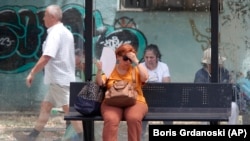 FILE - A woman tries to cool herself while waiting for a bus on a hot day in Skopje, North Macedonia, June 20, 2024. (AP Photo/Boris Grdanoski)
