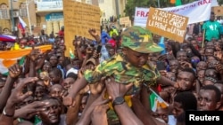 Men hold a child dressed in military uniform as they gather with thousands of anti-sanctions protesters in support of the putschist soldiers in the capital Niamey, Niger, Aug. 3, 2023.