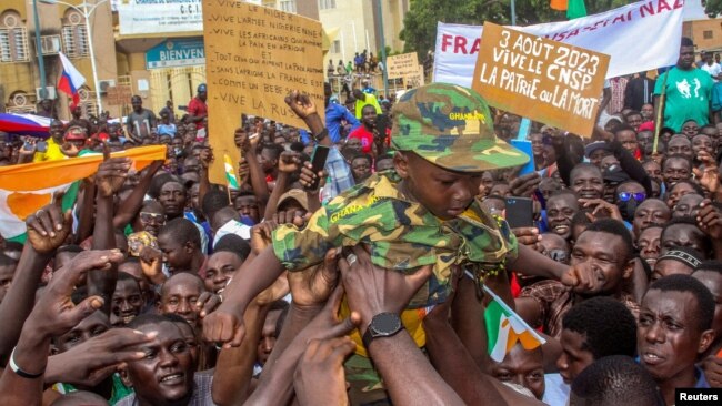 Men hold a child dressed in military uniform as they gather with thousands of anti-sanctions protesters in support of the putschist soldiers in the capital Niamey, Niger, Aug. 3, 2023.