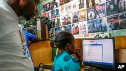 FILE - An Internet cafe owner, left, stands nearby as a customer, right, uses a computer at an internet cafe in the Kibera neighborhood of Nairobi, Kenya, Sept. 29, 2021. 