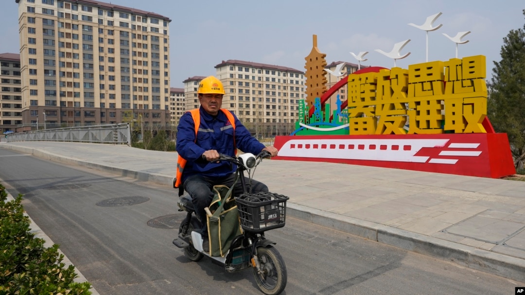 中国河北雄安街头一名工人骑车路过一处口号宣传牌。（2023年4月1日）