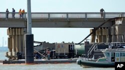 Para pekerja memeriksa lokasi di mana sebuah tongkang menabrak struktur jembatan Pulau Pelican di Galveston, Texas, pada 15 Mei 2024. (Foto: AP/David J. Phillip)