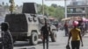 FILE - People walk past an armored police vehicle patrolling the streets in Port-au-Prince, July 15, 2024. 