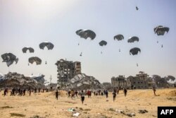 Arhiva - Ljudi trče ka paketima humanitarne pomoći izbačenim iz aviona nedaleko od uništenih zgrada u severnom delu Pojasa Gaze, 23. aprila 2024.