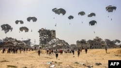 FILE — People rush toward humanitarian aid packages dropped near destroyed buildings in the northern Gaza Strip, April 23, 2024, amid the ongoing conflict in the Palestinian territory between Israel and the militant group Hamas.