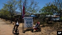 FILE - A girl rides her bike past an anti-tourist sign in Lahaina, Hawaii, Aug. 17, 2023.
