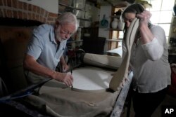 Ned Heywood cuts out the initial shape from a rolled slab of clay as Julia Land takes away the excess during the making of an English Heritage Blue Plaque, at Heritage Ceramics, The Workshop Gallery in Chepstow, Wales, Sept. 6, 2023.