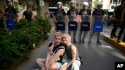 Two people sit next to a line of police officers blocking a street during the LGBTQ Pride March in Istanbul, Turkey, June 25, 2023.