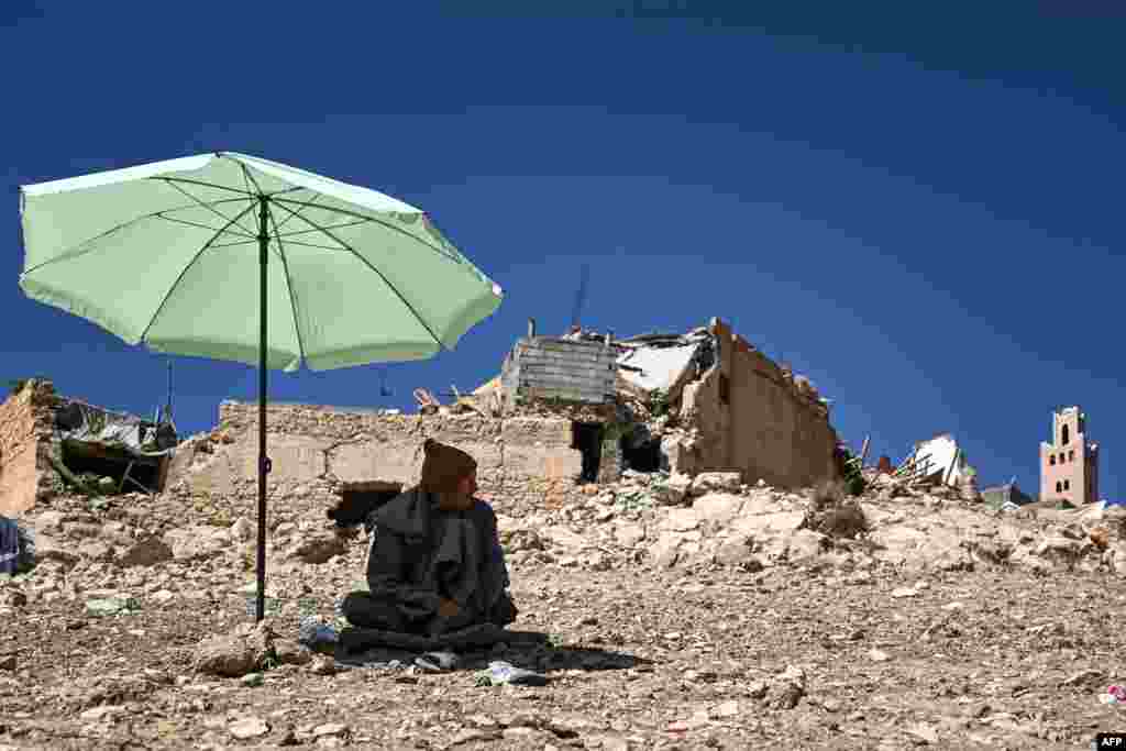 A resident sits in the shade of an umbrella near a mosque and buildings damaged by the September 8 earthquake in the village of Moulay Brahim in al-Haouz province in the High Atlas mountains of central Morocco.