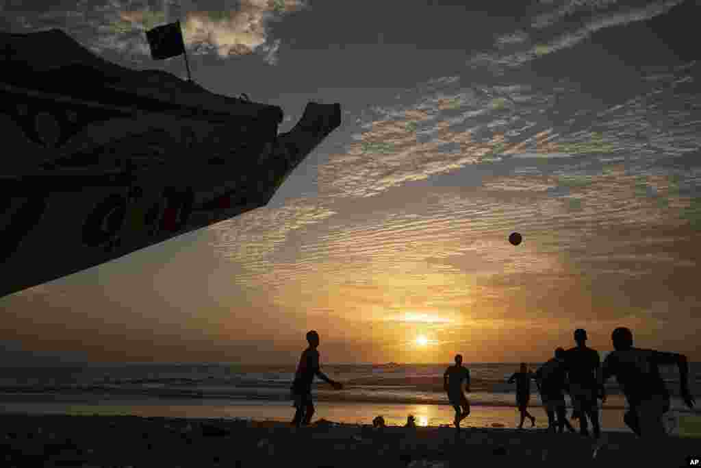 Silhouetted against the setting sun, youths play soccer next to a pirogue docked on the beach in Saint Louis, Senegal, Thursday, January 19, 2023.