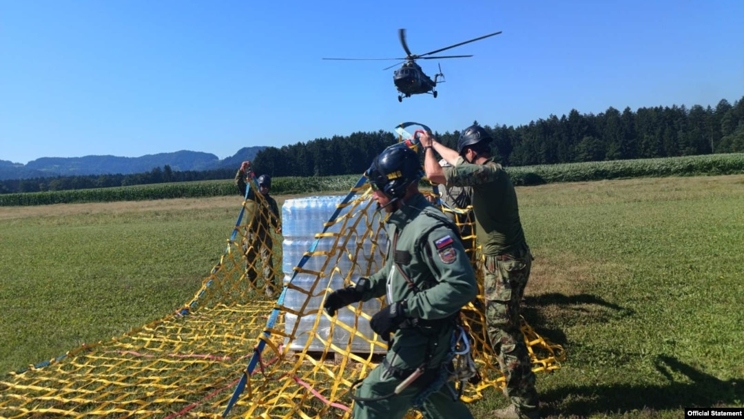 Pripadnici oružanih snaga Slovenije poripremaju pakete sa vodom namenjene stanovnicima poplavama pogođenih krajeva zemlje, dok se helikopter Vojske Srbije priprema za preuzimanje tereta, na fotografiji koju je objavilo Ministarstvo odbrane Srbije, 14. avgusta 2023.