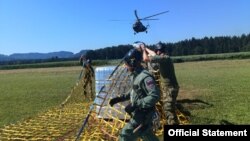 Pripadnici oružanih snaga Slovenije poripremaju pakete sa vodom namenjene stanovnicima poplavama pogođenih krajeva zemlje, dok se helikopter Vojske Srbije priprema za preuzimanje tereta, na fotografiji koju je objavilo Ministarstvo odbrane Srbije, 14. avgusta 2023.