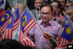 Perdana Menteri Malaysia Anwar Ibrahim mengibarkan bendera nasional usai menyampaikan pidatonya pada Hari Nasional di Putrajaya, Malaysia, Rabu, 30 Agustus 2023. (Foto: AP) ​