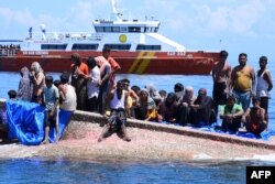 Pengungsi Rohingya menunggu untuk diselamatkan dari lambung kapal mereka yang terbalik saat kapal Badan Pencarian dan Pertolongan Nasional (BASARNAS) mendekat di perairan sekitar 16 mil laut (29 kilometer) lepas pantai barat Aceh, 21 Maret 2024. (Zahlul AKBAR/AFP)