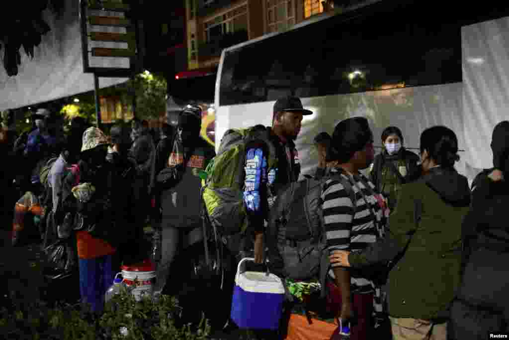 Miembros del Instituto Nacional de Migración observan cómo migrantes&nbsp;abordan un autobús en el parque Giordano Bruno para ser trasladados a un albergue, en Ciudad de México.