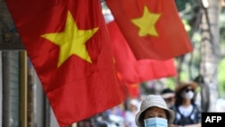 FILE - Women walk past Vietnam national flags hoisted along a street in Hanoi on May 18, 2020. Concern is growing over a purported internal Vietnamese directive which is said to order government agencies to increase surveillance of citizens and crack down on civil society.