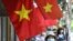 FILE - Women walk past Vietnam national flags hoisted along a street in Hanoi on May 18, 2020. Concern is growing over a purported internal Vietnamese directive which is said to order government agencies to increase surveillance of citizens and crack down on civil society.