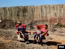 Palestinians sit in armchairs flanked by an Israeli separation wall, in this part of a series called "Occupied Pleasures," by artist Tanya Habjouqa, at the Arab World Institute in Paris, through Nov. 19, 2023. (Lisa Bryant/VOA)