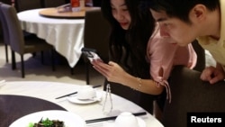 Para pelanggan tampk memfoto menu pasta tinta cumi yang ditaburi jangkrik di restoran House of Seafood di Singapura, pada 16 Juli 2024. (Foto: Reuters/Edgar Su)