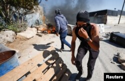 A Palestinian covers his face during clashes with Israeli troops after Israeli settlers attack Umm Safa village near Ramallah, in the Israeli-occupied West Bank, June 24, 2023.