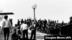 ARCHIVO - Un grupo de jóvenes se agrupa alrededor de una persona herida mientras miembros de la Guardia Nacional de Ohio, con máscaras antigás, sostienen sus armas al fondo en el campus de la Universidad Estatal de Kent en Kent, Ohio, el 4 de mayo de 1970.