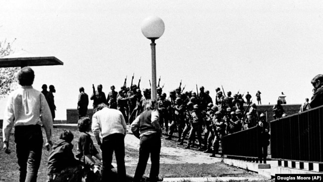 ARCHIVO - Un grupo de jóvenes se agrupa alrededor de una persona herida mientras miembros de la Guardia Nacional de Ohio, con máscaras antigás, sostienen sus armas al fondo en el campus de la Universidad Estatal de Kent en Kent, Ohio, el 4 de mayo de 1970.