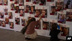 FILE - A woman touches photos of Israelis missing and held captive in Gaza, displayed on a wall in Tel Aviv on Oct. 21, 2023.