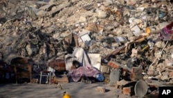 Seorang pria tidur di depan bangunan yang hancur di Kahramanmaras, tenggara Turki, 13 Februari 2023. (Foto: AP)