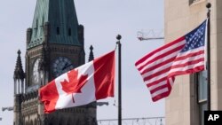 FILE - The Canadian and US flags are displayed on lampposts March 22, 2023, near Parliament Hill in Ottawa, Ontario. 