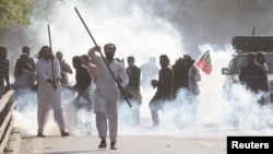 Supporters of former Prime Minister Imran Khan react amid tear gas smoke fired by the police to disperse them during clashes, in Lahore, Pakistan, March 8, 2023.