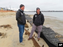 Tim Dillingham, left, and Capt. Al Modjeski, right, of the American Littoral Society, examine logs of coconut husk known as coir along the bank of the Shark River in Neptune, N.J., Jan. 31, 2023. (AP Photo/Wayne Parry)