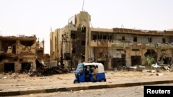 People pass by damaged cars and buildings at the central market during clashes between the paramilitary Rapid Support Forces and the army in Khartoum North, Sudan, April 27, 2023. 