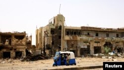 People pass by damaged cars and buildings at the central market during clashes between the paramilitary Rapid Support Forces and the army in Khartoum North, Sudan.