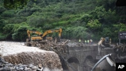 Ekskavator tampak beroperasi membersihkan puing-puing dari sebuah jembatan menyusul banjir yang menerjang desa Xinhua, di Ya'an, provinsi Sichuan, China, pada 21 Juli 2024. (Foto: Wang Xi/Xinhua via AP)