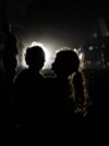 A Palestinian girl holding a child is silhouetted in against the lights of an oncoming car in Rafah, in the southern Gaza Strip, on May 4, 2024.