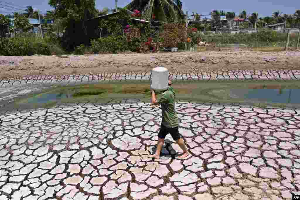 A man carries a plastic bucket across the cracked bed of a parched dried-up pond in Vietnam&#39;s southern Ben Tre province, March 19, 2024.