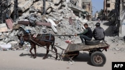 Palestinian boys ride a donkey-pulled cart near a building destroyed in Israeli bombardment in Rafah, in the southern Gaza Strip, March 31, 2024.
