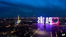 A visitor strolls past a "Paris" sign that is reflected in the glass wall of the Montparnasse tower observation deck as the Eiffel Tower stands in the background, ahead of the 2024 Summer Olympics, in Paris, France, July 23, 2024.