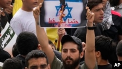 Seorang pendukung Hizbullah mengangkat plakat berbahasa Arab yang bertuliskan:"Ia pasti akan jatuh," dalam protes untuk menunjukkan solidaritas mereka terhadap Palestina, di pinggiran selatan Beirut, Lebanon, Jumat, 13 Oktober 2023. (Foto: AP )