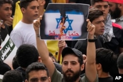 Seorang pendukung Hizbullah mengangkat plakat berbahasa Arab yang bertuliskan:"Ia pasti akan jatuh," dalam protes untuk menunjukkan solidaritas mereka terhadap Palestina, di pinggiran selatan Beirut, Lebanon, Jumat, 13 Oktober 2023. (AP/Hussein Malla)