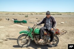 A man poses for a photo on his motorcycle next to his desert home while guarding the lands and destroyed houses that have been abandoned after the drying up of the Aral Sea, outside Muynak, Uzbekistan, June 24, 2023.