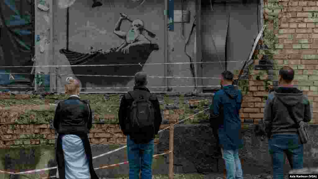 Rusiya ordusunun atdığı bomba ilə dağıdılmış yaşayış binasının divarında britaniyalı rəssam Benksinin çəkdiyi əsəri izləməyə gəlmiş insanlar.&nbsp;Borodyanka, Xarkiv vilayəti, Ukrayna. &nbsp;
