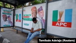 FILE — A man sits at a bus stop decorated with electoral campaign posters of All Progressives Congress Presidential candidate, Bola Tinubu, with his running mate Kashim Shettima, ahead of Nigeria's Presidential election, in Lagos, Jan. 31, 2023.