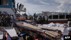 Des volontaires déchargent des cercueils apportés par le gouvernement central de la RDC, après des inondations et des glissements de terrain déclenchés par de fortes pluies, à Nyamukubi, dans l'est du pays, le 9 mai 2023. (Photo Guerchom Ndebo / AFP)