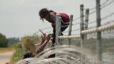 Migrants who crossed the Rio Grande from Mexico into the U.S. climb a fence with barbed wire and concertina wire, Aug. 21, 2023, in Eagle Pass, Texas. 