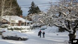 La gente camina por una calle cubierta de nieve en el vecindario de Grant Park en Portland, Oregon, el jueves 23 de febrero de 2023. La ciudad experimentó su segundo día con más nieve registrado. (Foto AP/Drew Callister)