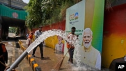 Municipal workers wash a side walk near a billboard featuring Indian Prime Minister Narendra Modi ahead of this week's summit of the Group of 20 nations, in New Delhi, India, Sept. 7, 2023.