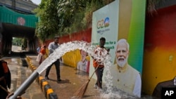 Pekerja kota mencuci jalan dekat papan reklame yang menampilkan Perdana Menteri India Narendra Modi menjelang KTT negara-negara Kelompok 20 minggu ini, di New Delhi, India.