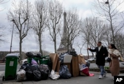 People walk past a pile of garbage near the Eiffel Tower in Paris, March 12, 2023, as strikes continue with uncollected garbage piling higher by the day. (AP Photo/Michel Euler, File)